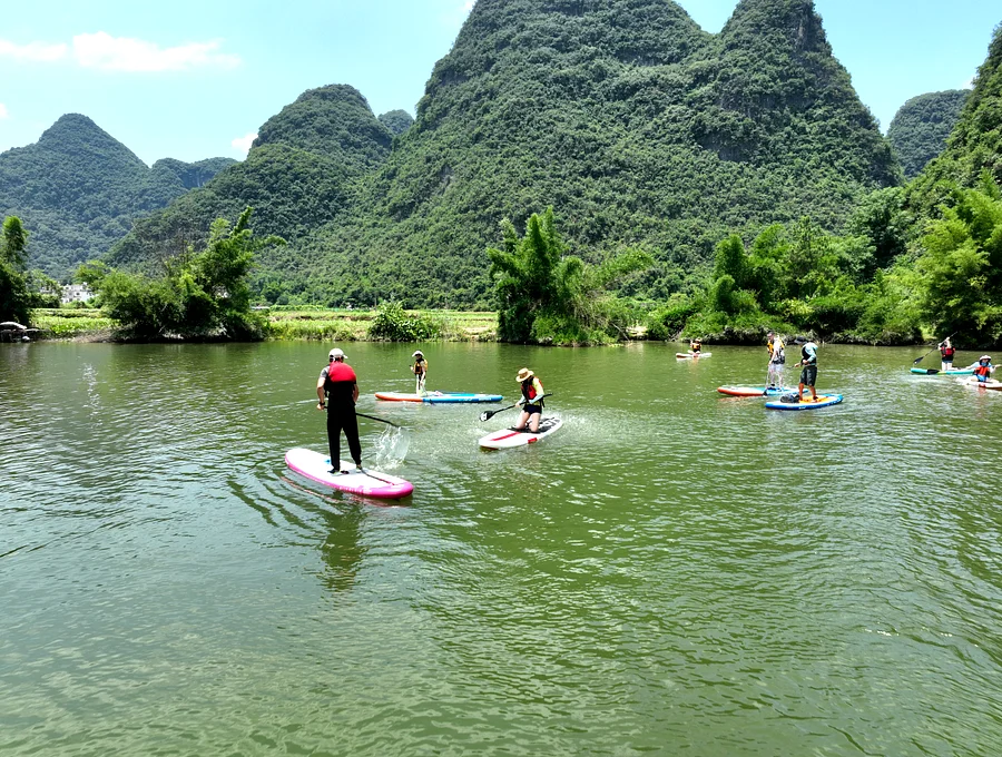 Group paddleboarding on the Yulong River with karst peaks in the background, Yangshuo China