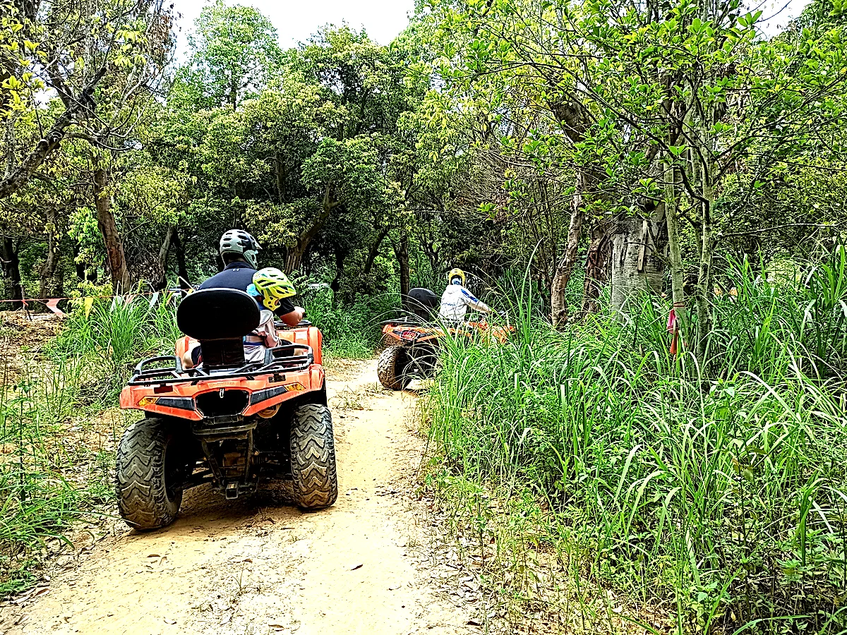 Two families riding orange ATVs along a forest trail through lush vegetation in the Guangxi countryside, China