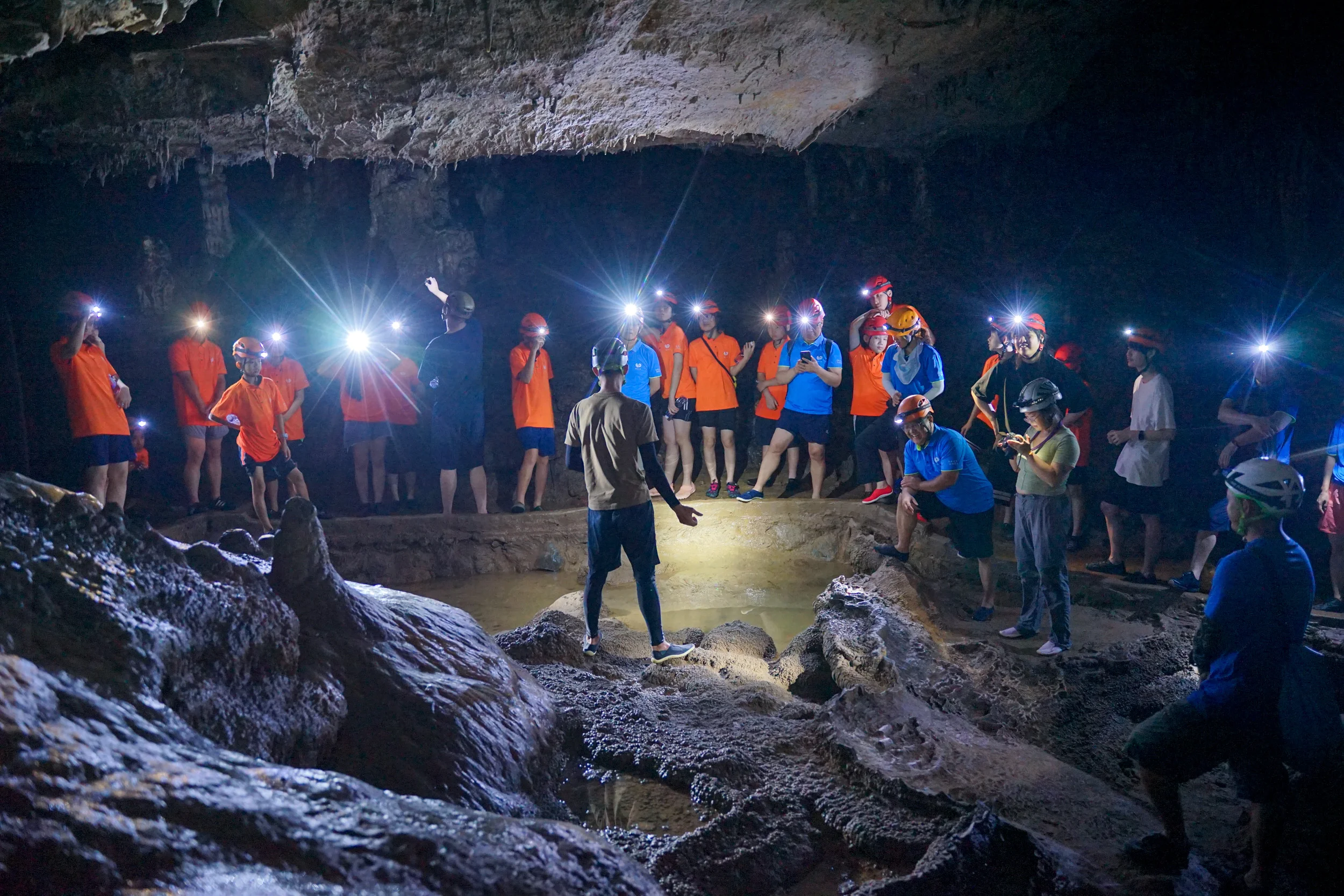 Guide explaining cave formations to a group of helmeted explorers inside a karst cave in China