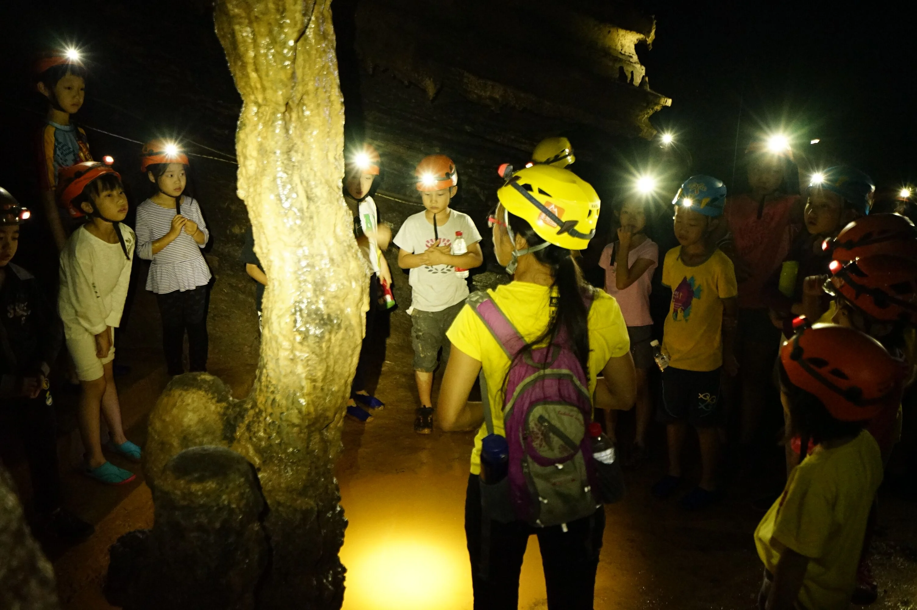 Group of explorers with headlamps observing dramatic stalactites in a Chinese karst cave