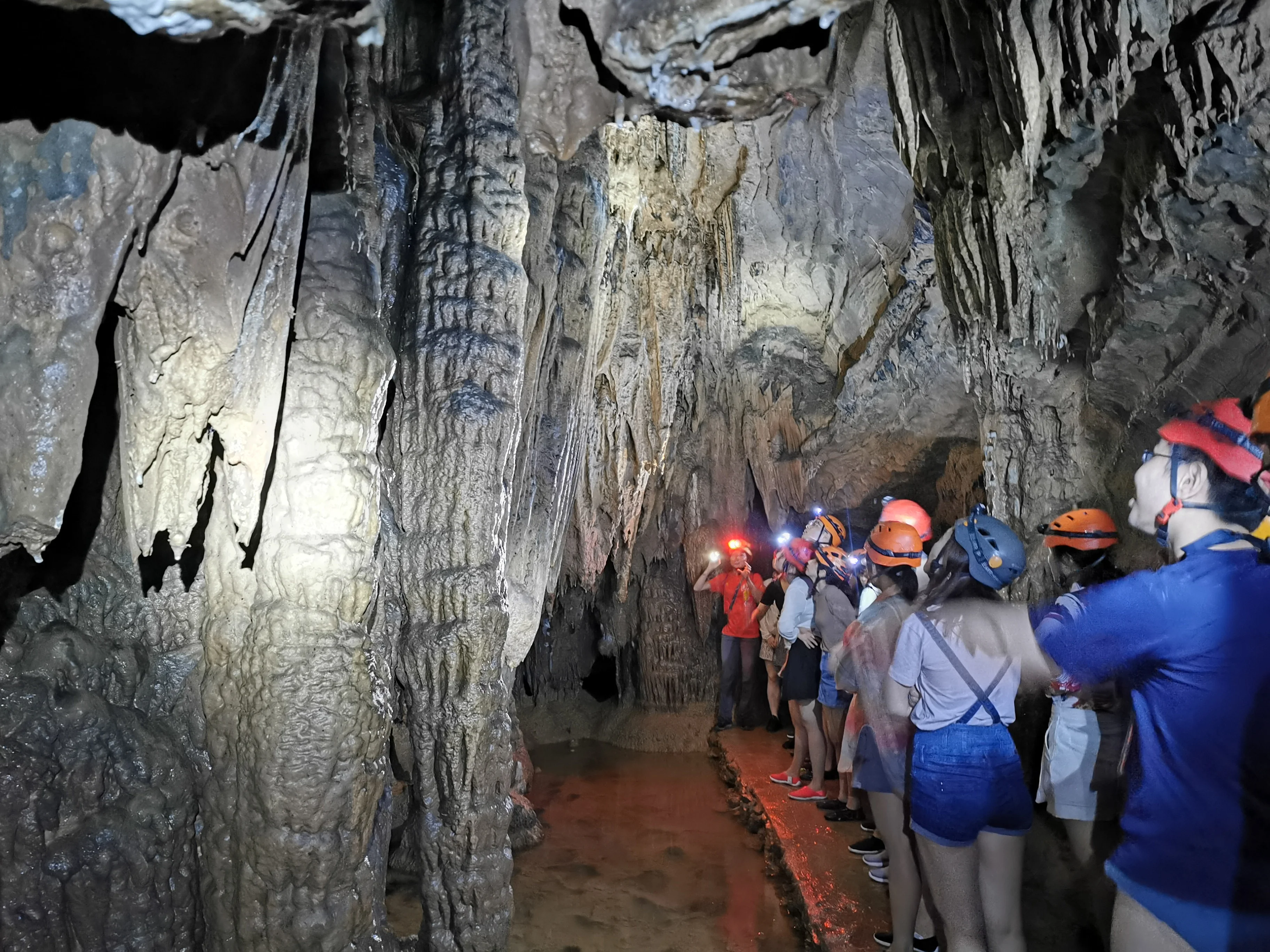 Caving team in orange helmets navigating stone steps beside an underground pool in China