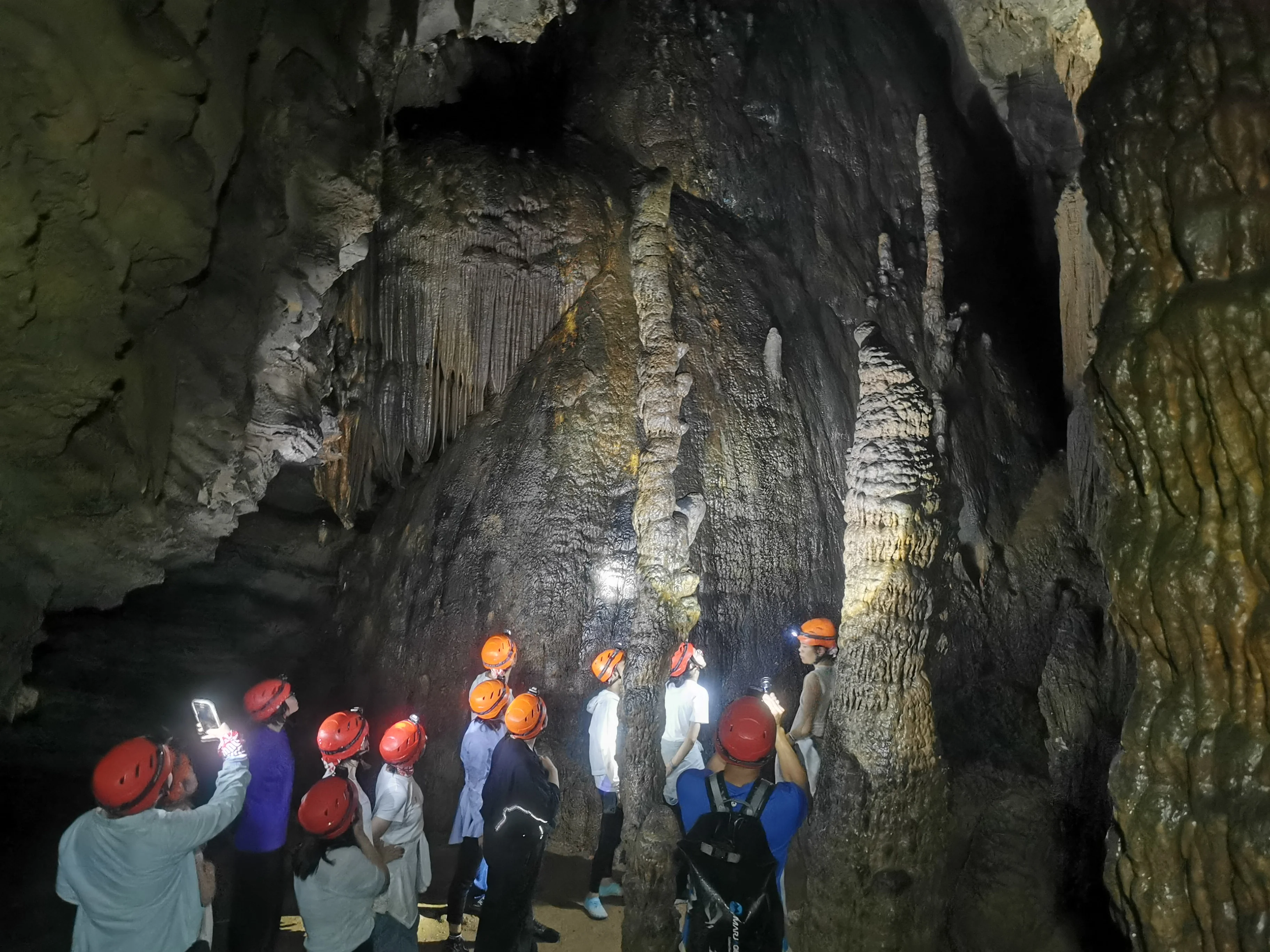 Explorers crouching through a low cave passage during a wild caving adventure in China