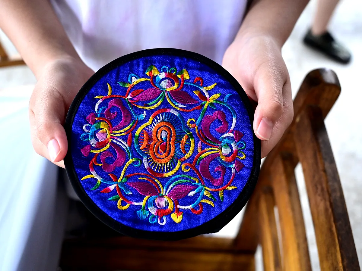Close-up of hands holding intricate colorful embroidered textile in a Guangxi minority village