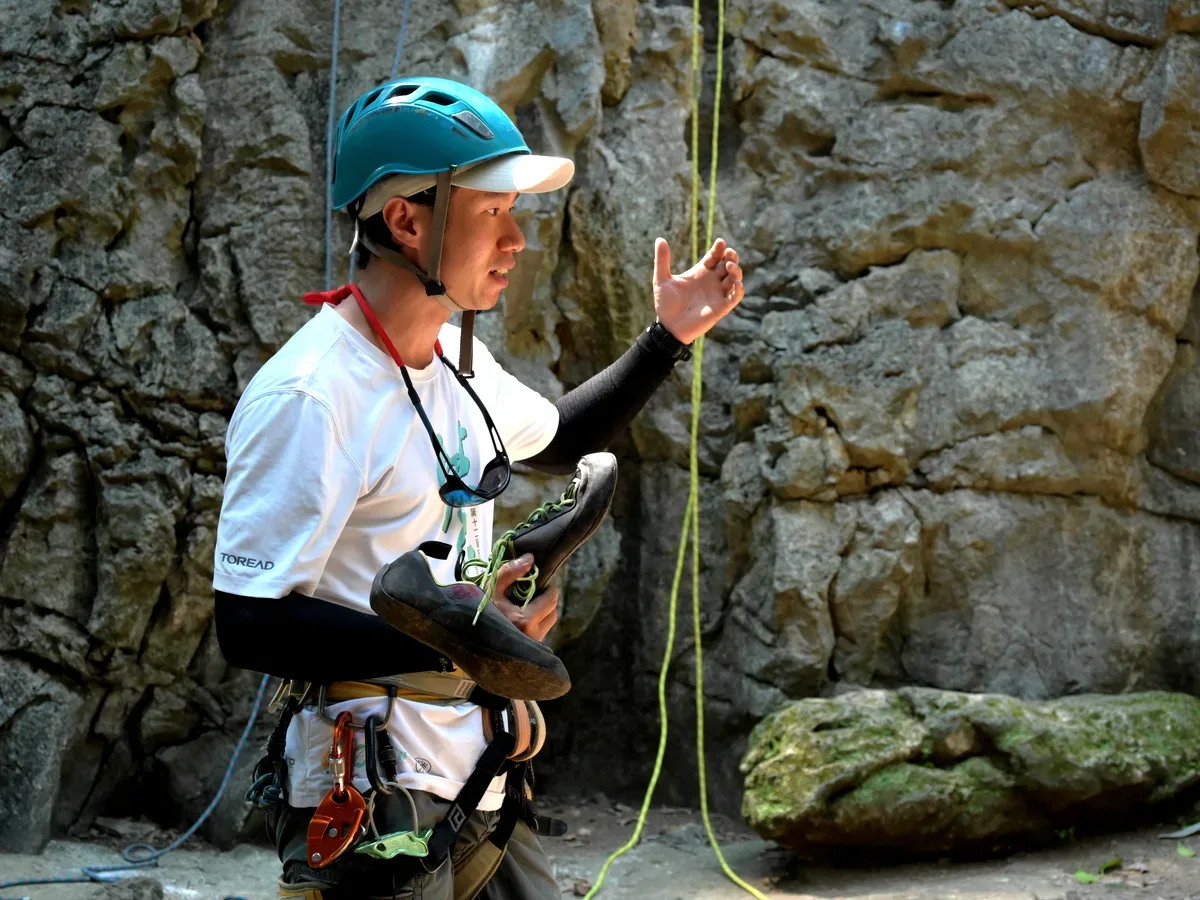Young beginner climbing a karst rock face in China with safety harness and helmet