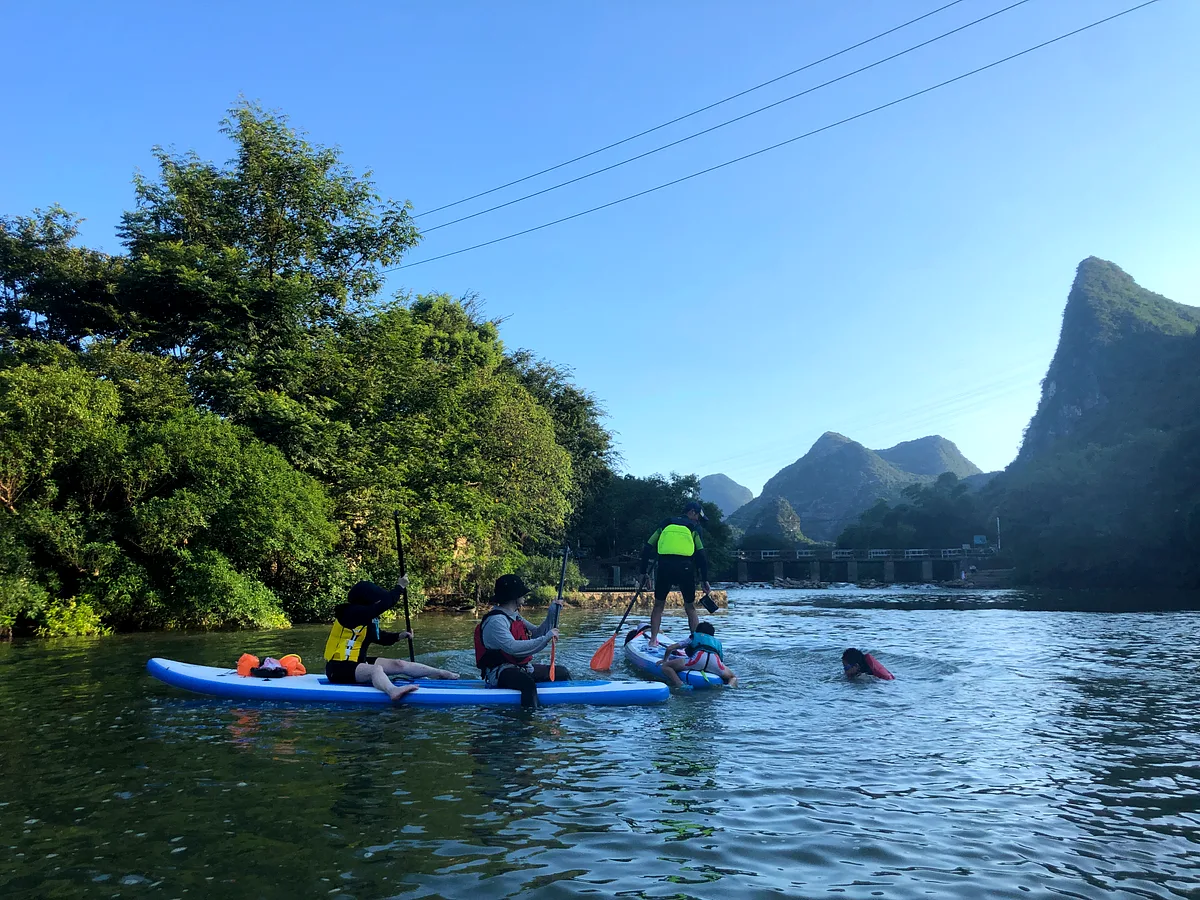 Family group on paddleboards, green mountains and a bridge in the background, China