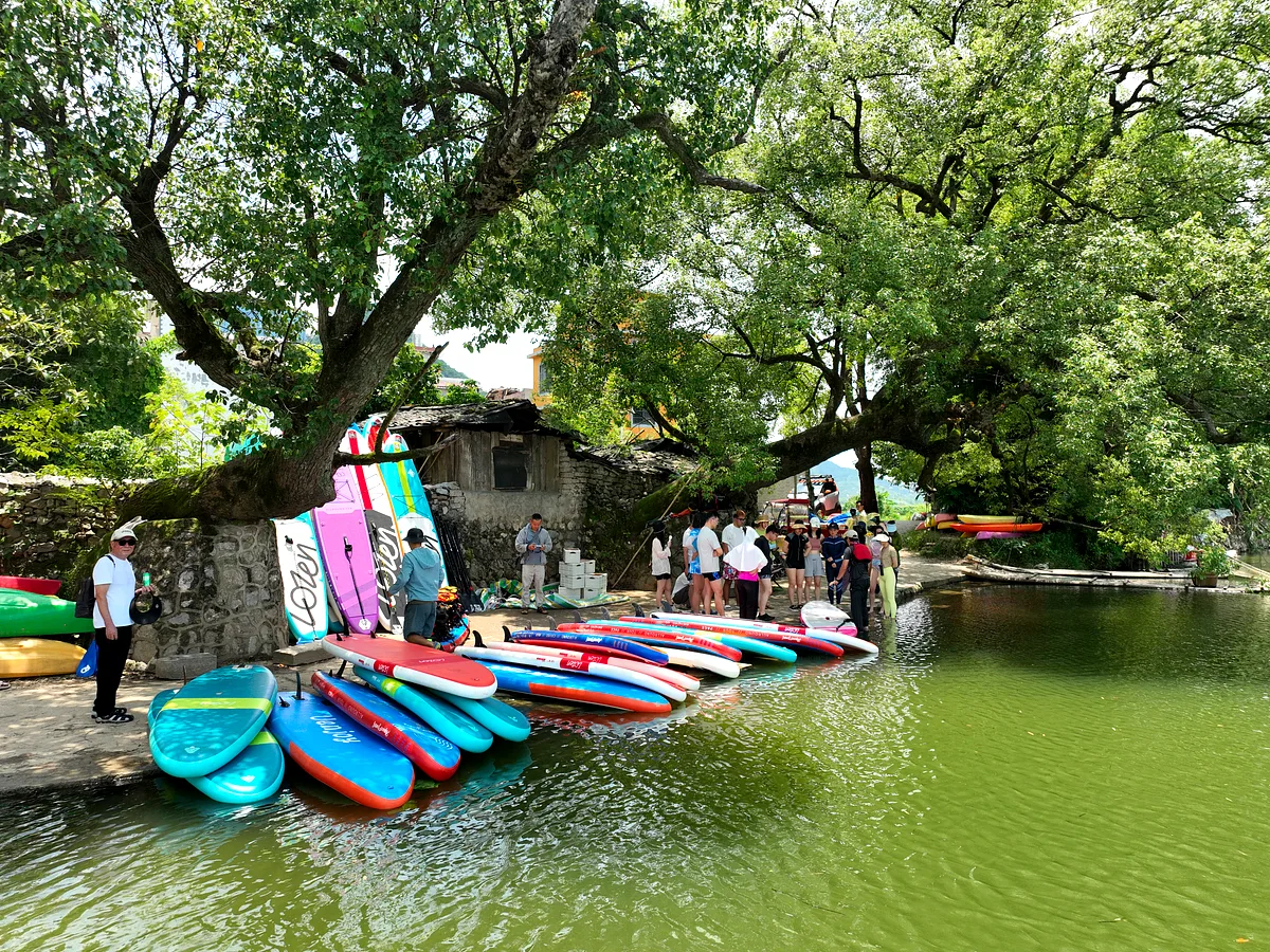 Group in life jackets paddleboarding on a calm river with lush karst mountains reflected in the water, China