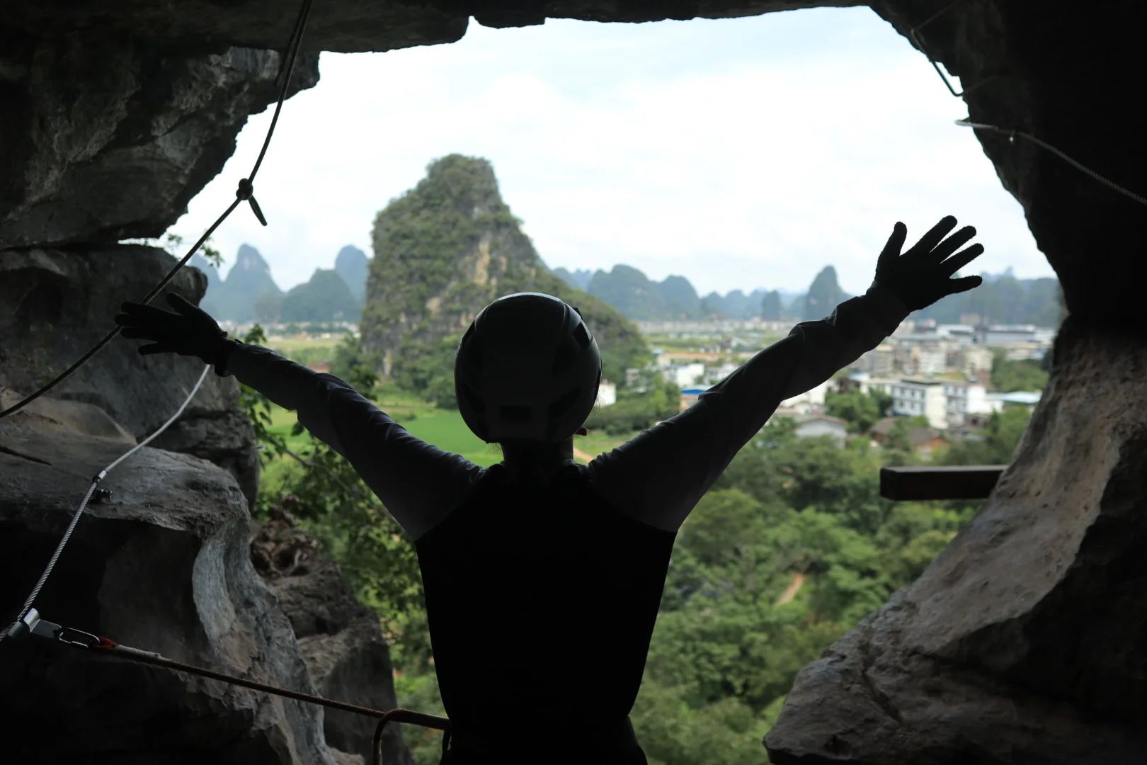 Woman with arms spread wide on a via ferrata cliff edge, karst mountains and valley behind her in China